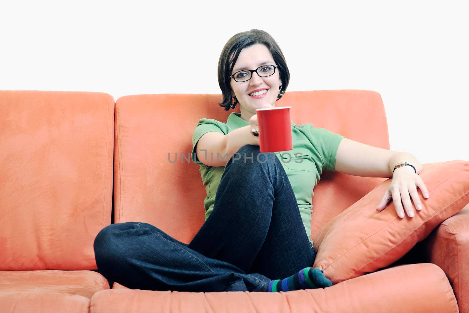 young happy woman drink coffee and holding red cup isolated on white on orange sofa