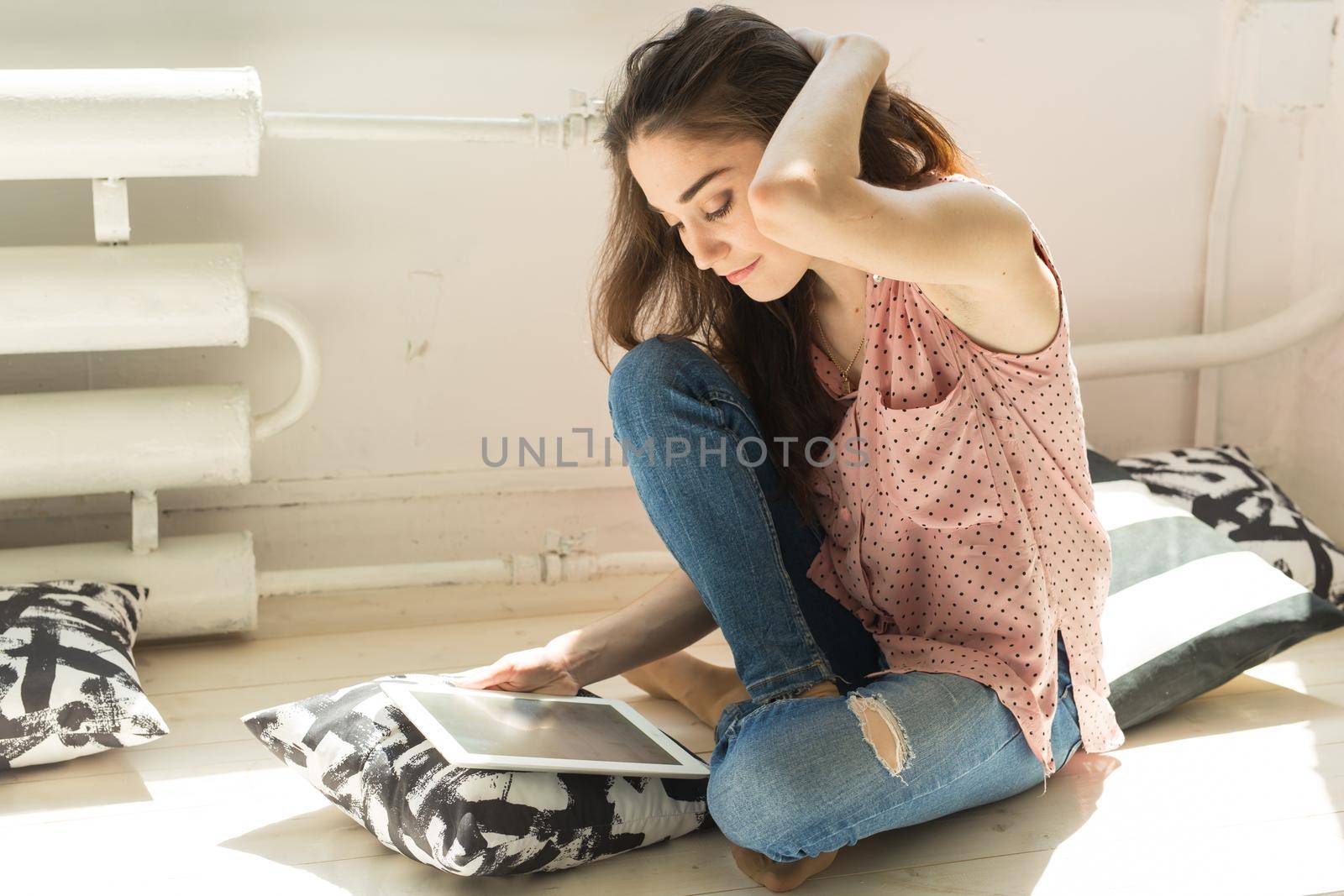 Technologies, people concept - young woman sitting on sofa and watching the tablet or surfing the net and smiling.