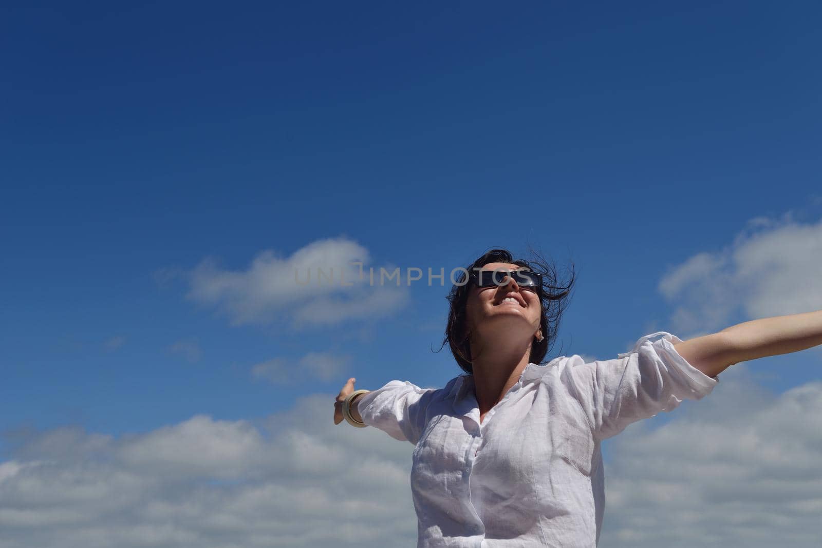 Happy  young woman with spreading arms, blue sky with clouds in background  - copyspace