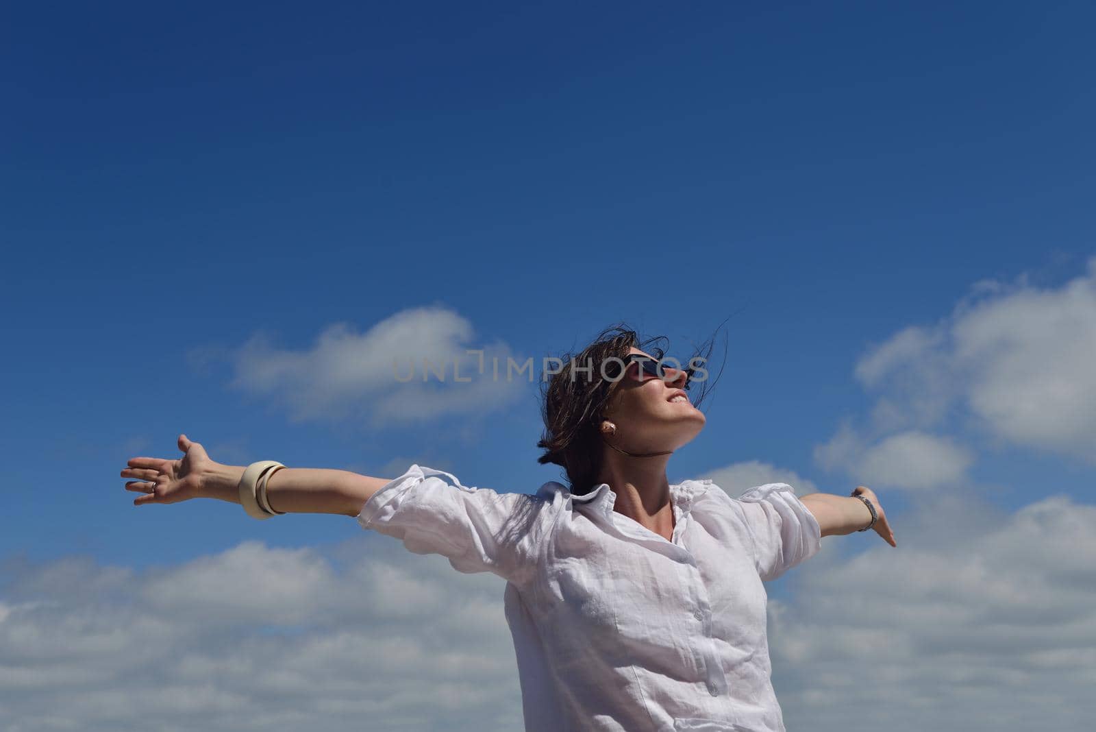 Happy  young woman with spreading arms, blue sky with clouds in background  - copyspace