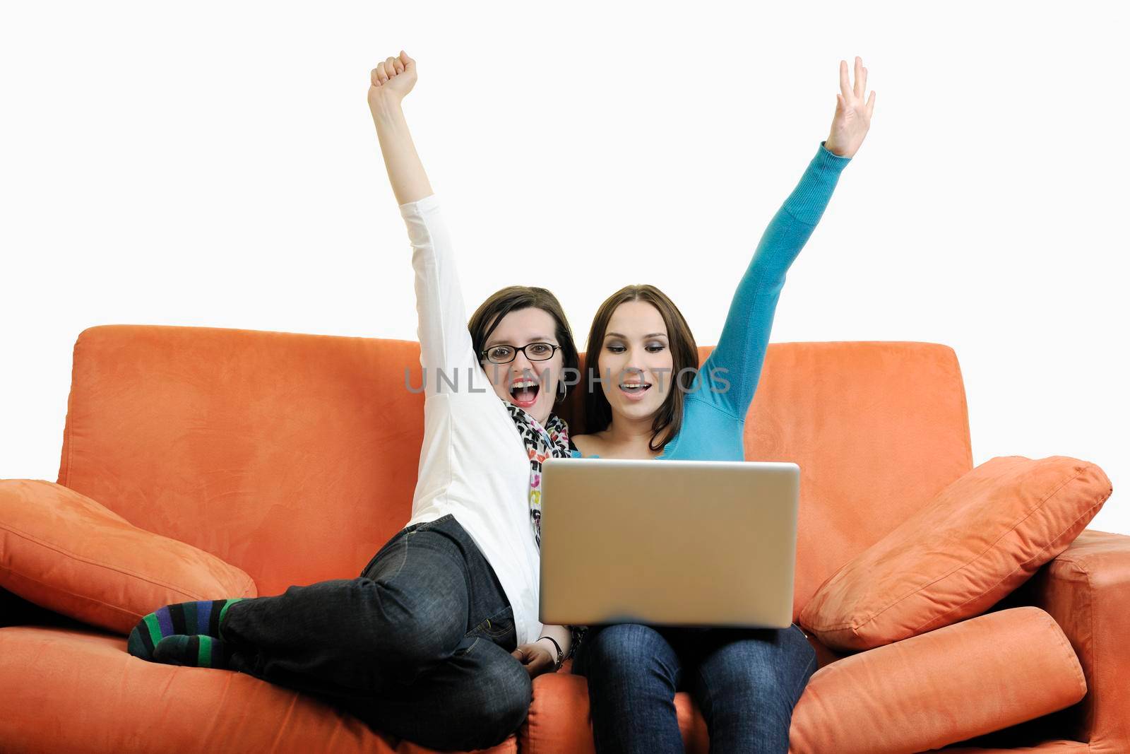 two happy young woman working on laptop computer on red sofa isolated on white