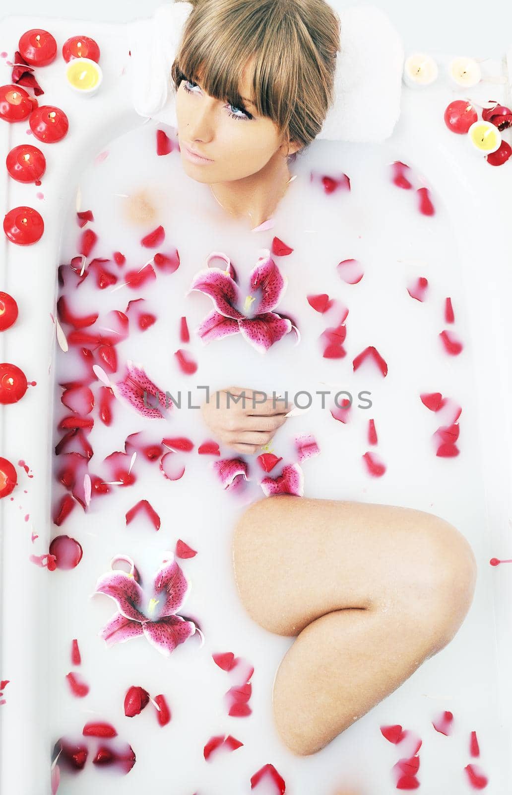 woman beauty spa and wellness treathment with red flower petals in bath with milk 