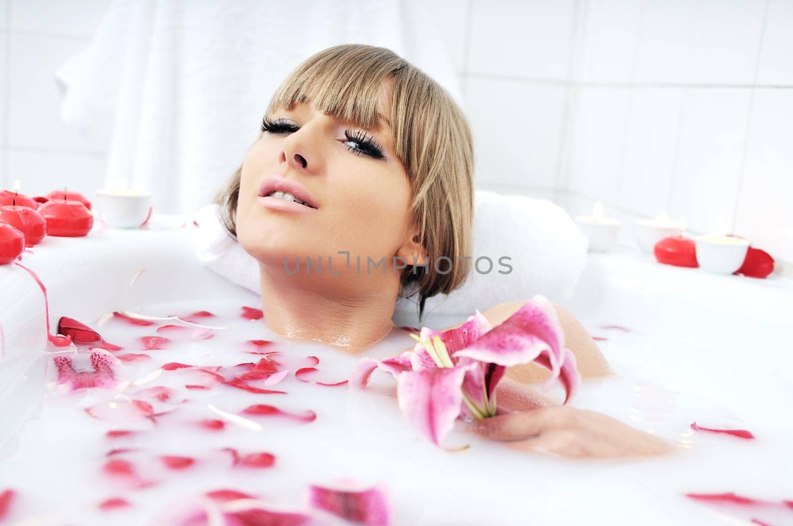 woman beauty spa and wellness treathment with red flower petals in bath with milk 