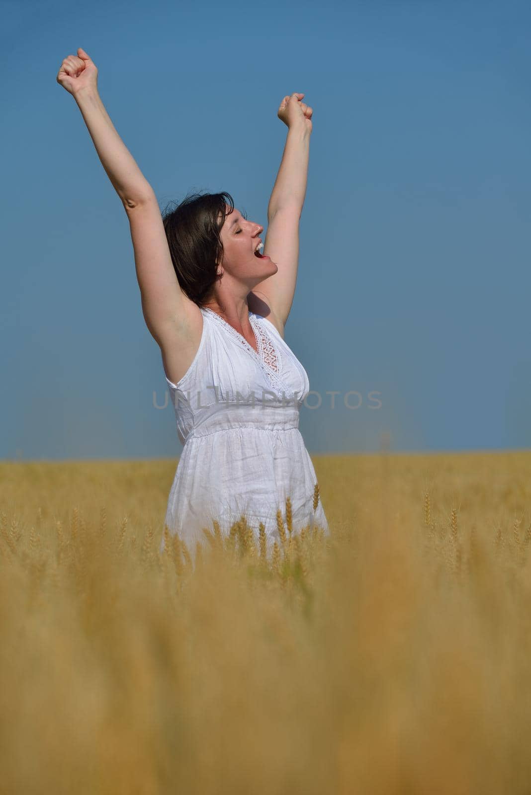 Young woman standing jumping and running  on a wheat field with blue sky the background at summer day representing healthy life and agriculture concept