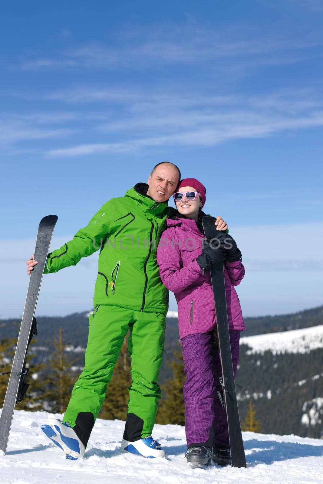 Portrait of happy couple at beautiful mountain on winter sunny day with blue sky and snow in background