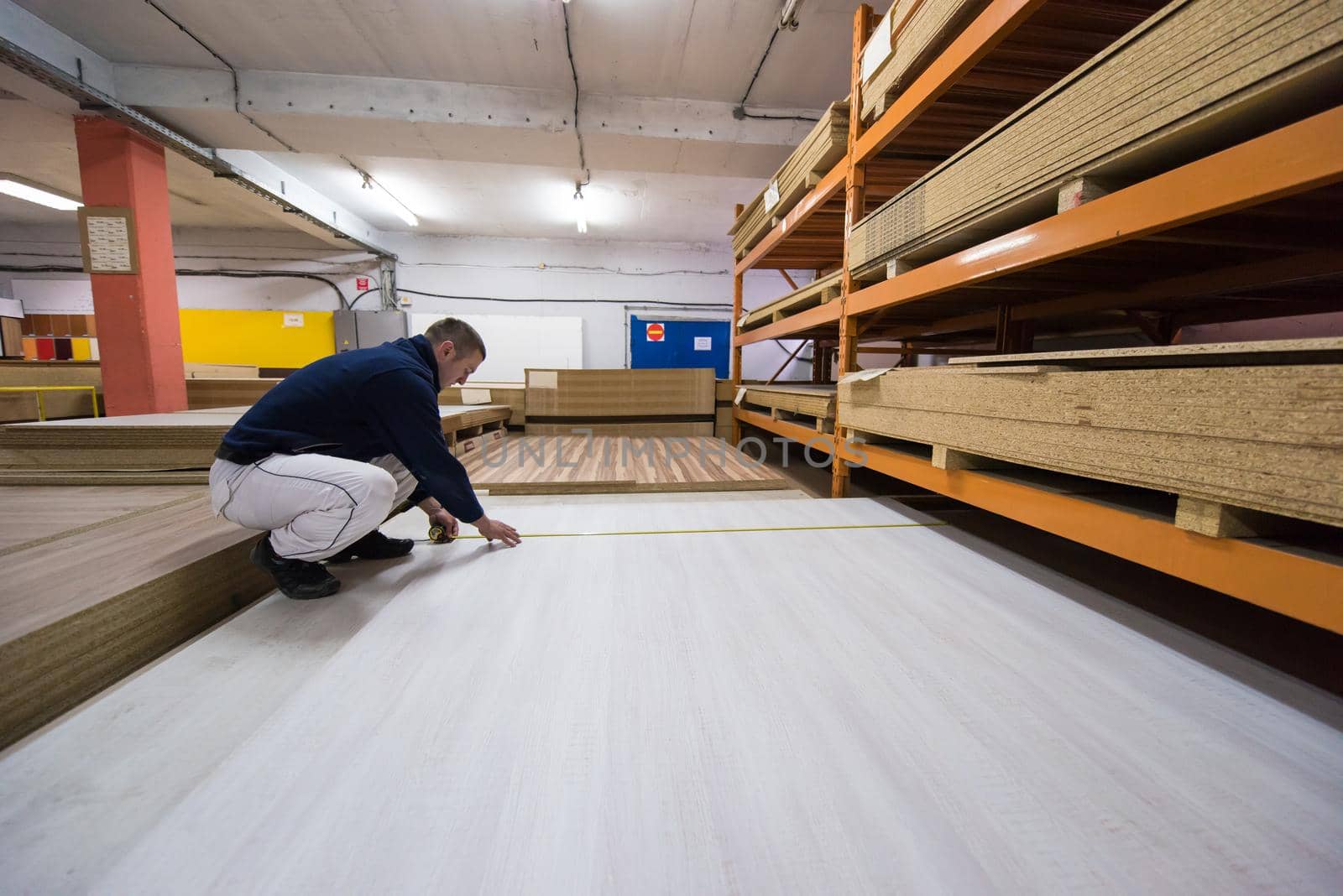 young man carpenter measuring wooden board for cutting while working in big modern carpentry High quality wood concept