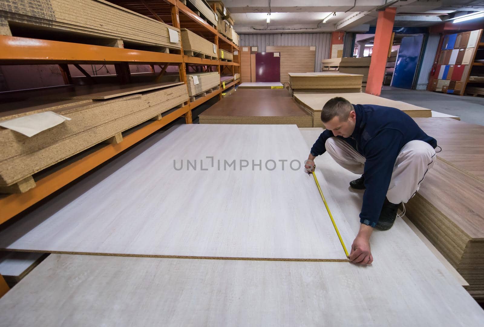 young man carpenter measuring wooden board for cutting while working in big modern carpentry High quality wood concept