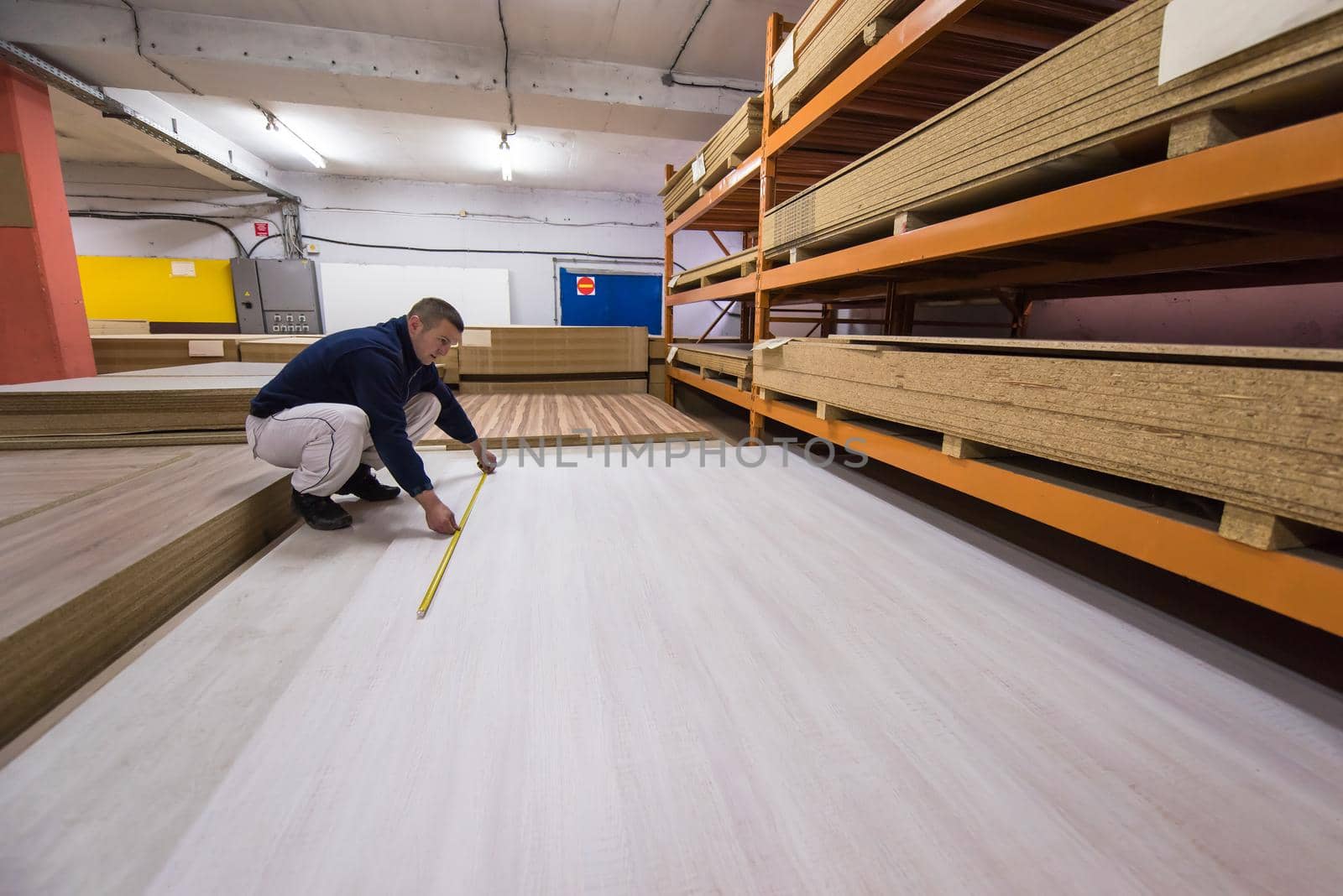 young man carpenter measuring wooden board for cutting while working in big modern carpentry High quality wood concept