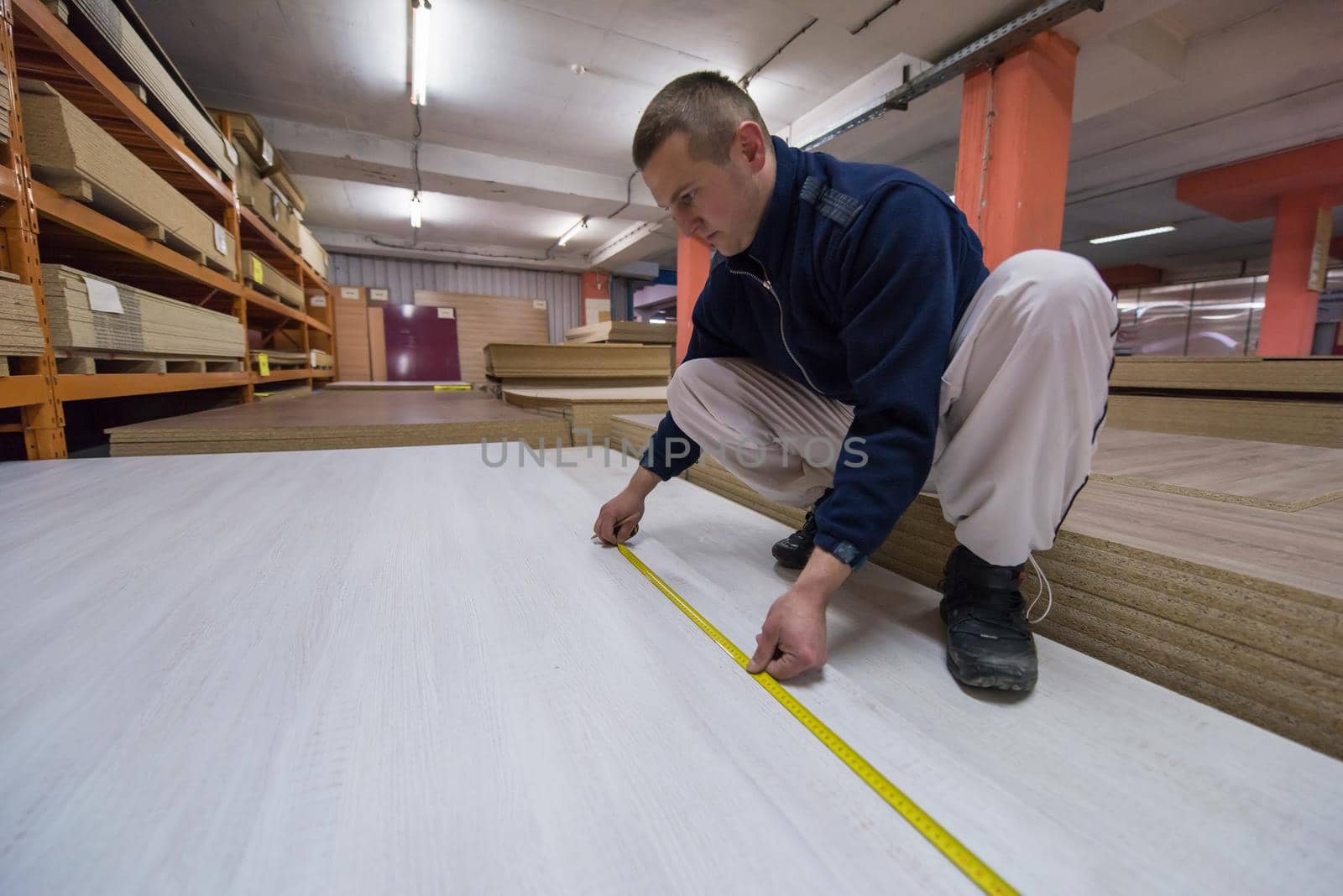 young man carpenter measuring wooden board for cutting while working in big modern carpentry High quality wood concept