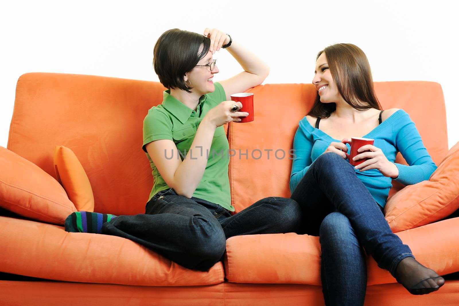 two young woman isolated on white with cup off coffee talking and chating isolated on whtie on orange sofa