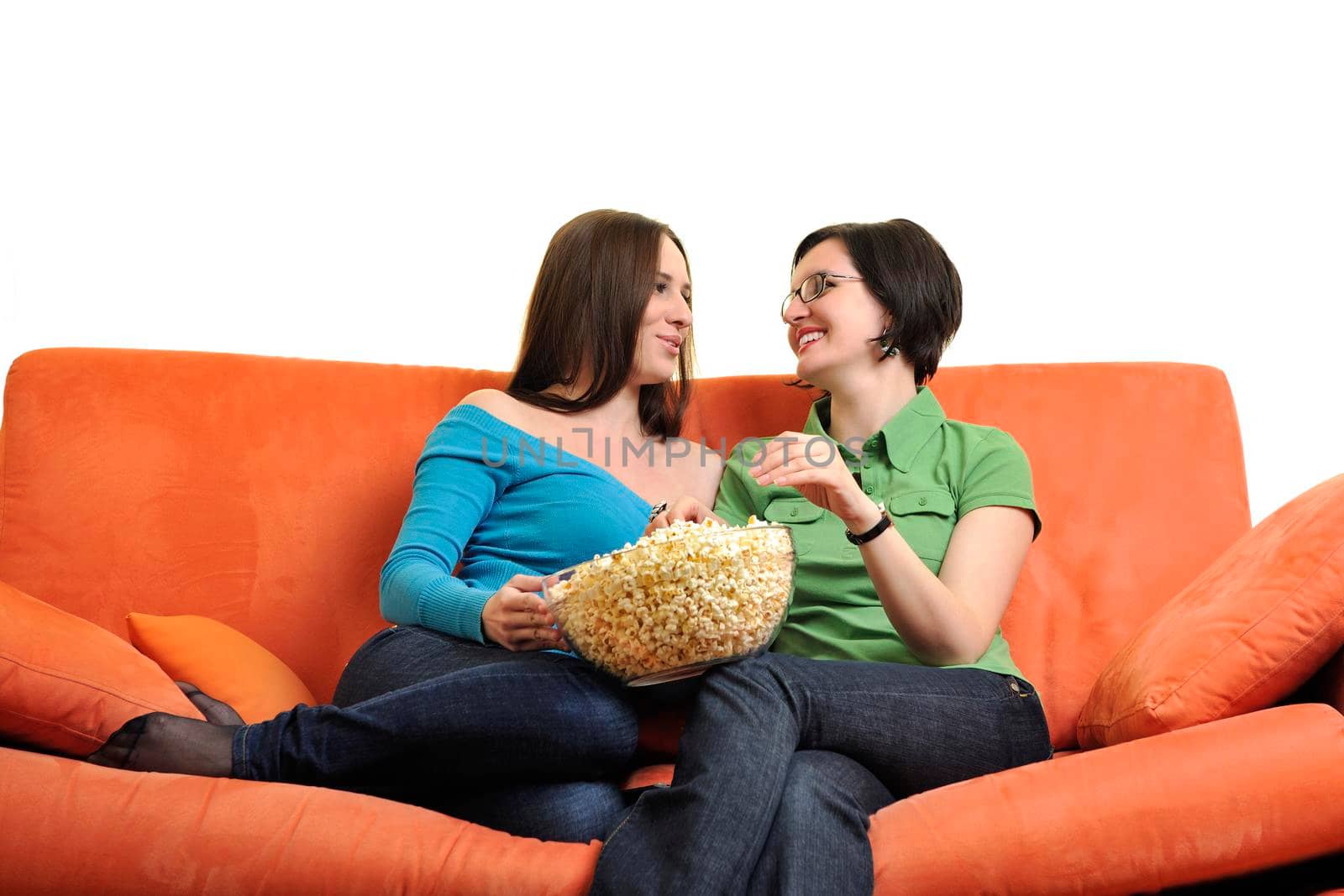 female friends eating popcorn and watching tv at home on orange sofa isolated on white