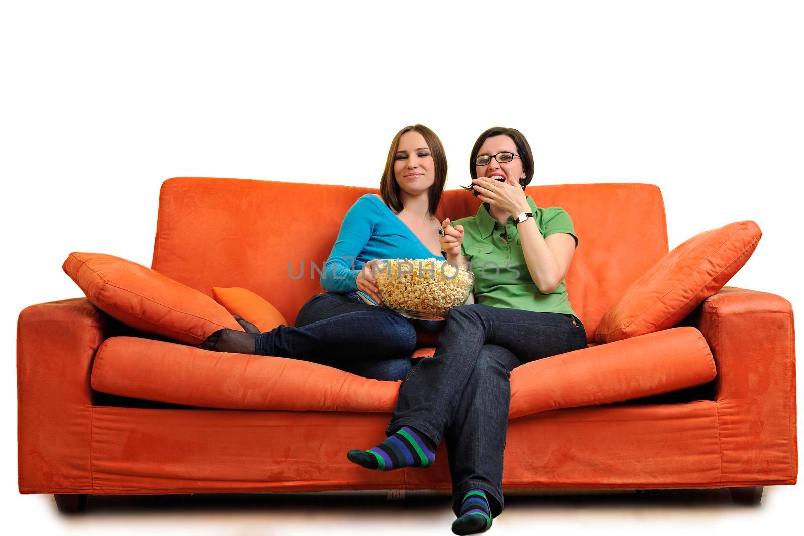 female friends eating popcorn and watching tv at home on orange sofa isolated on white