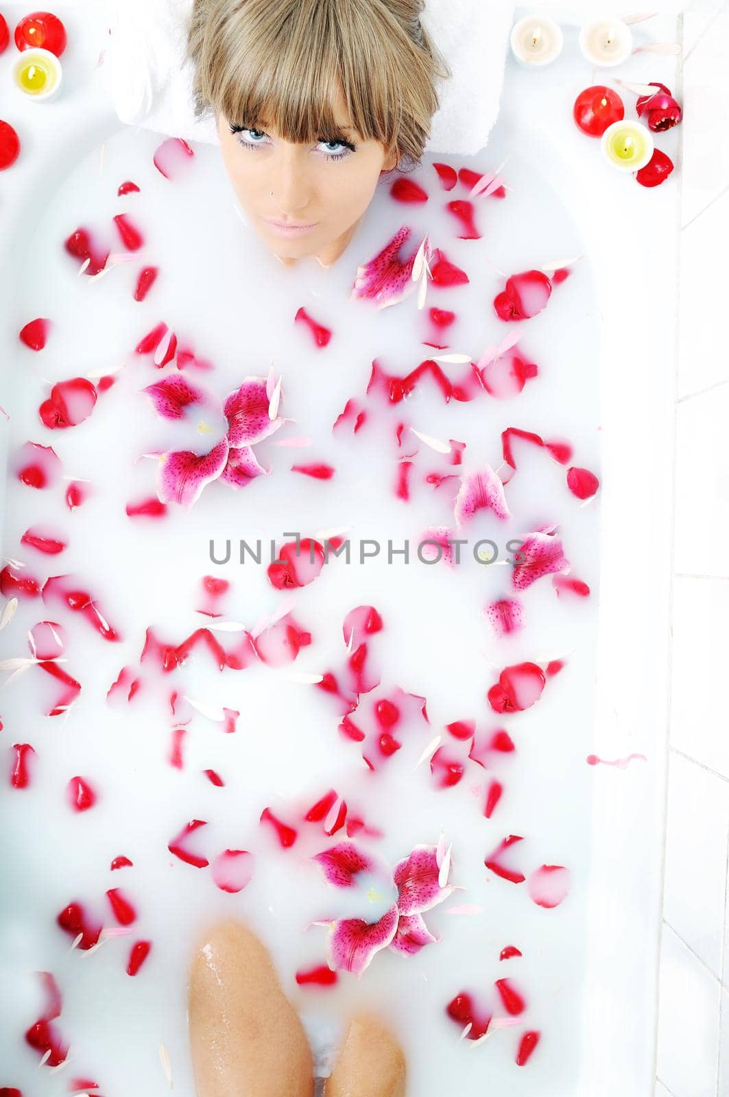 woman beauty spa and wellness treathment with red flower petals in bath with milk 