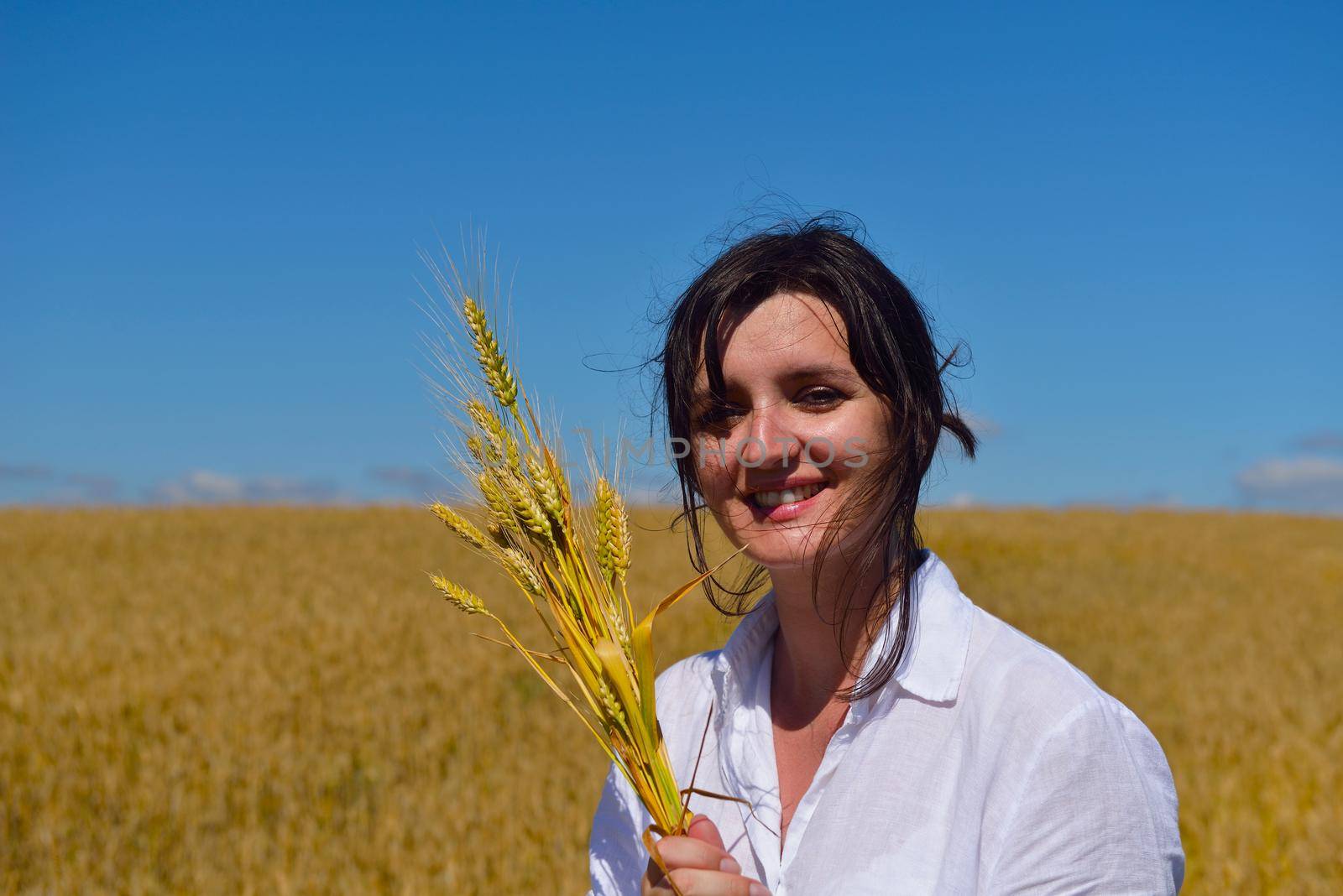 Young woman standing jumping and running  on a wheat field with blue sky the background at summer day representing healthy life and agriculture concept