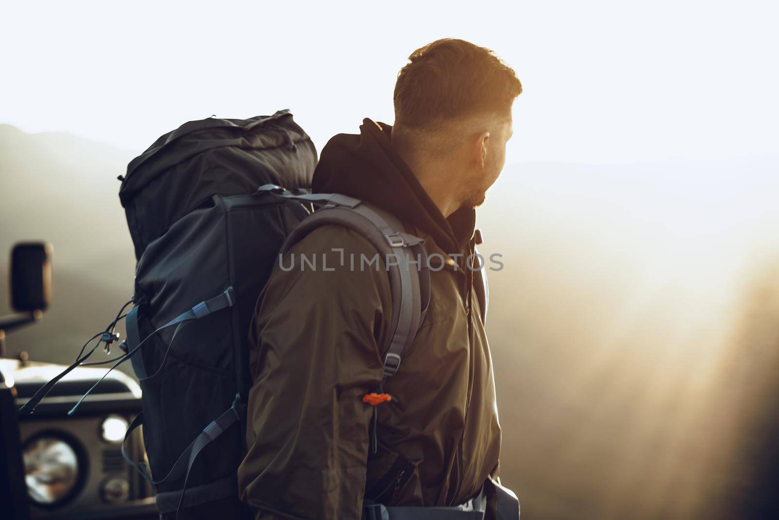Portrait of a young traveler man in hiking equipment standing near his off-road car at dawn
