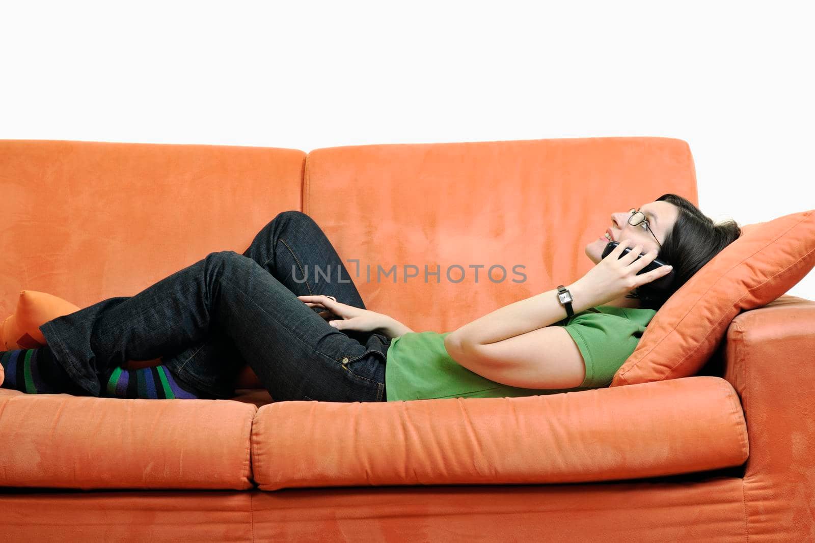 young woman on orange sofa talking by phone isolated on white in studio
