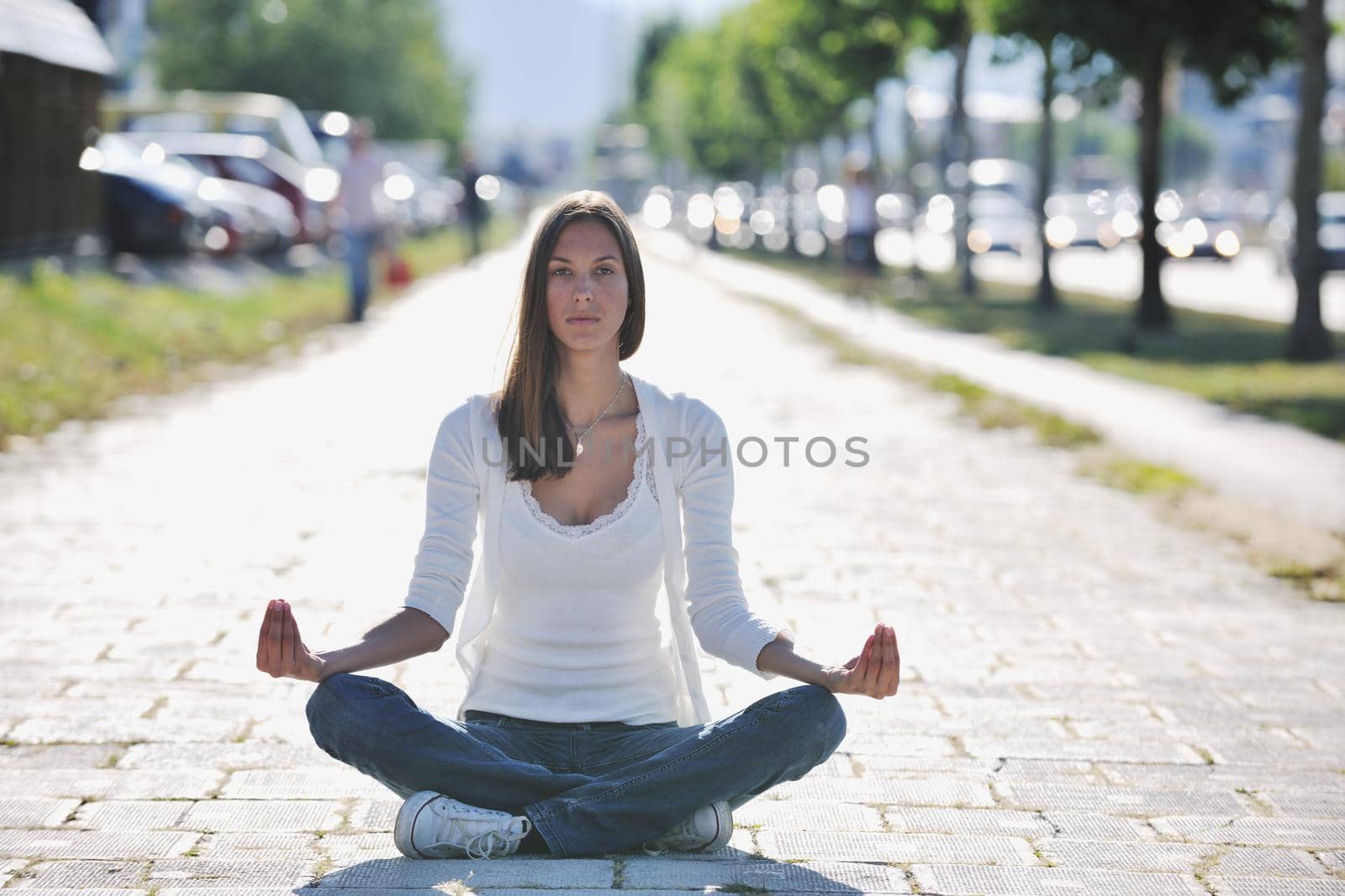 beautiful young woman meditating and exercise yoga in lotus position at street at beautiful sunny day with blured background