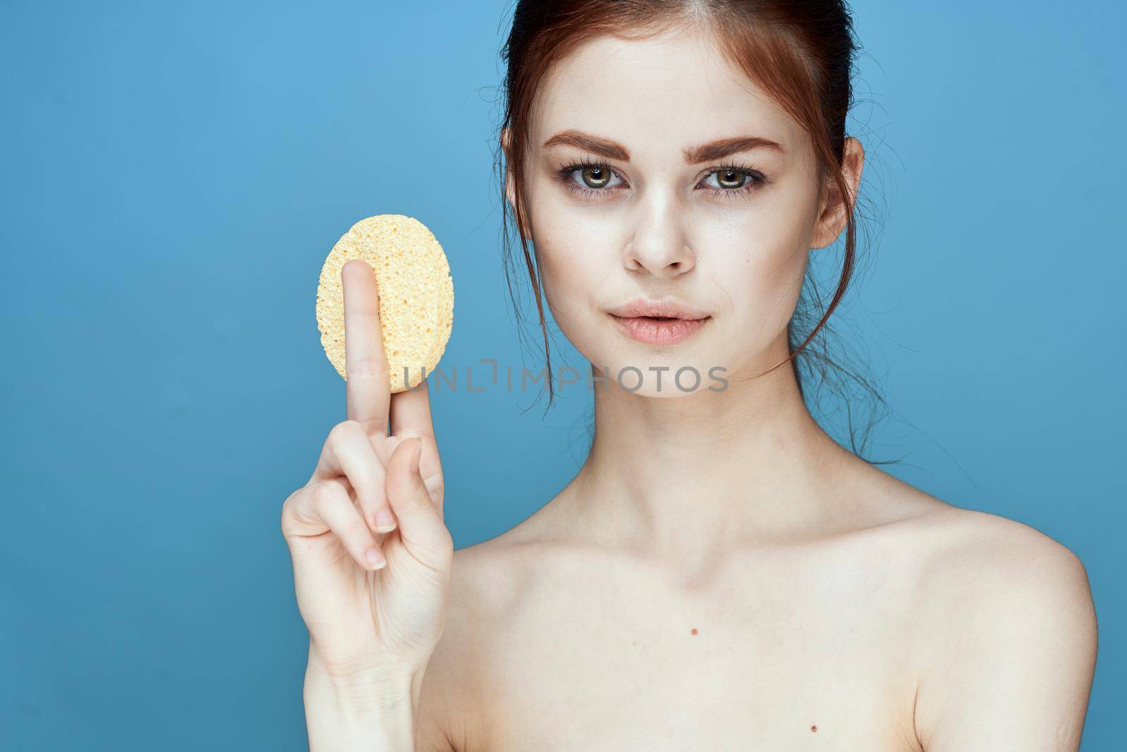 woman with sponges in hands bare shoulders clear skin blue background. High quality photo