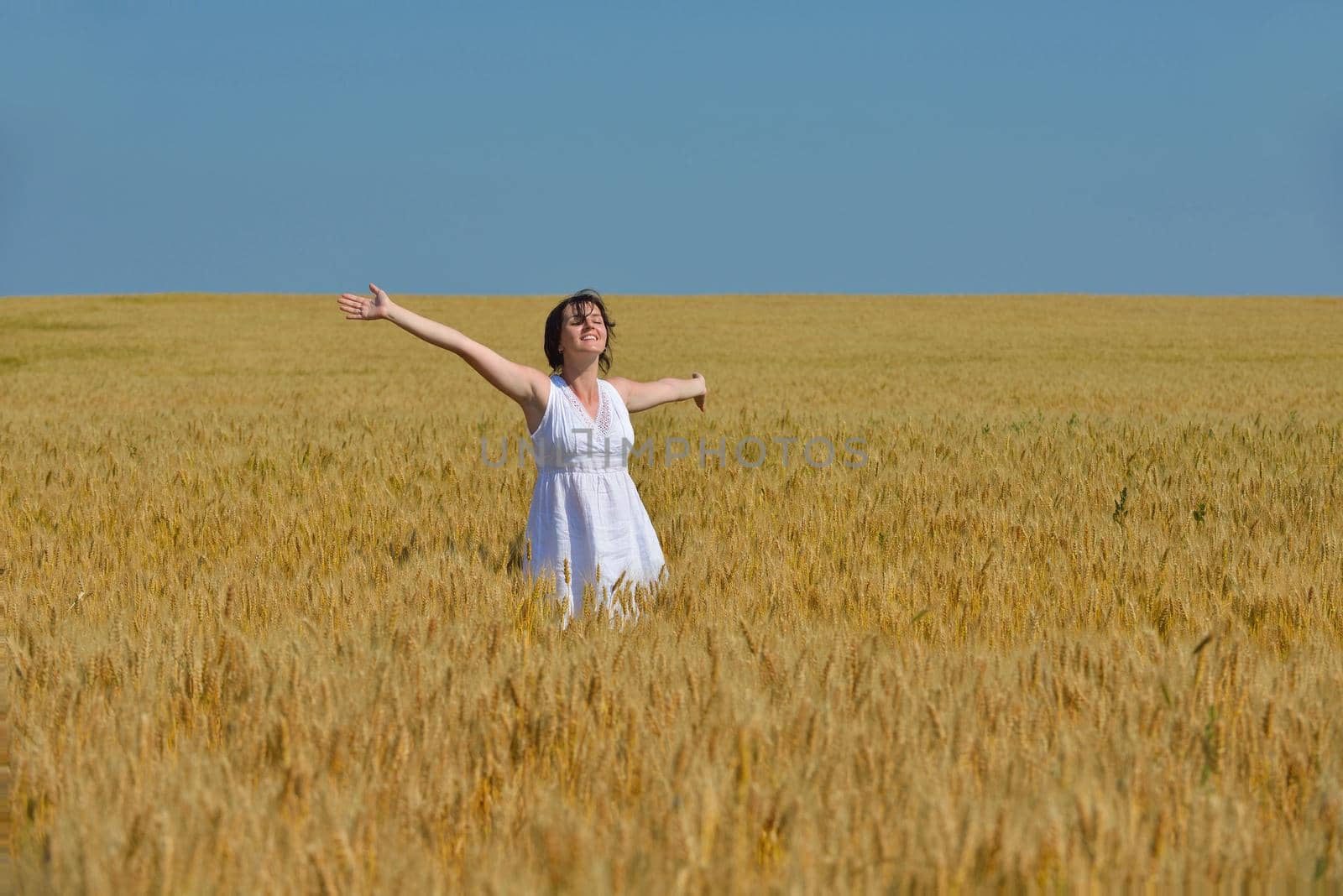 Young woman standing jumping and running  on a wheat field with blue sky in  background at summer day representing healthy life and agriculture concept