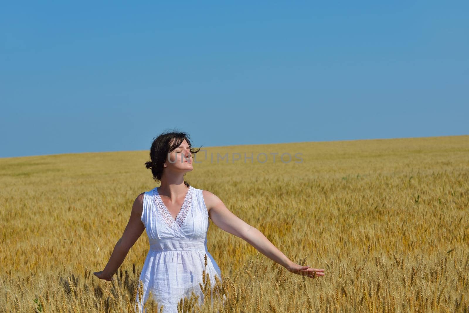 Young woman standing jumping and running  on a wheat field with blue sky in  background at summer day representing healthy life and agriculture concept
