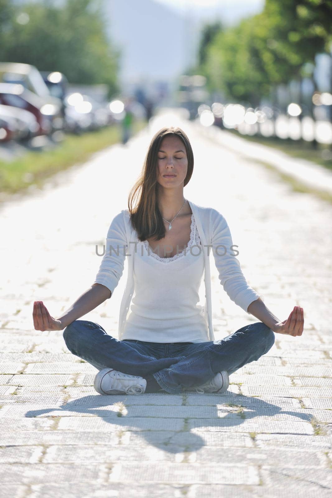 beautiful young woman meditating and exercise yoga in lotus position at street at beautiful sunny day with blured background