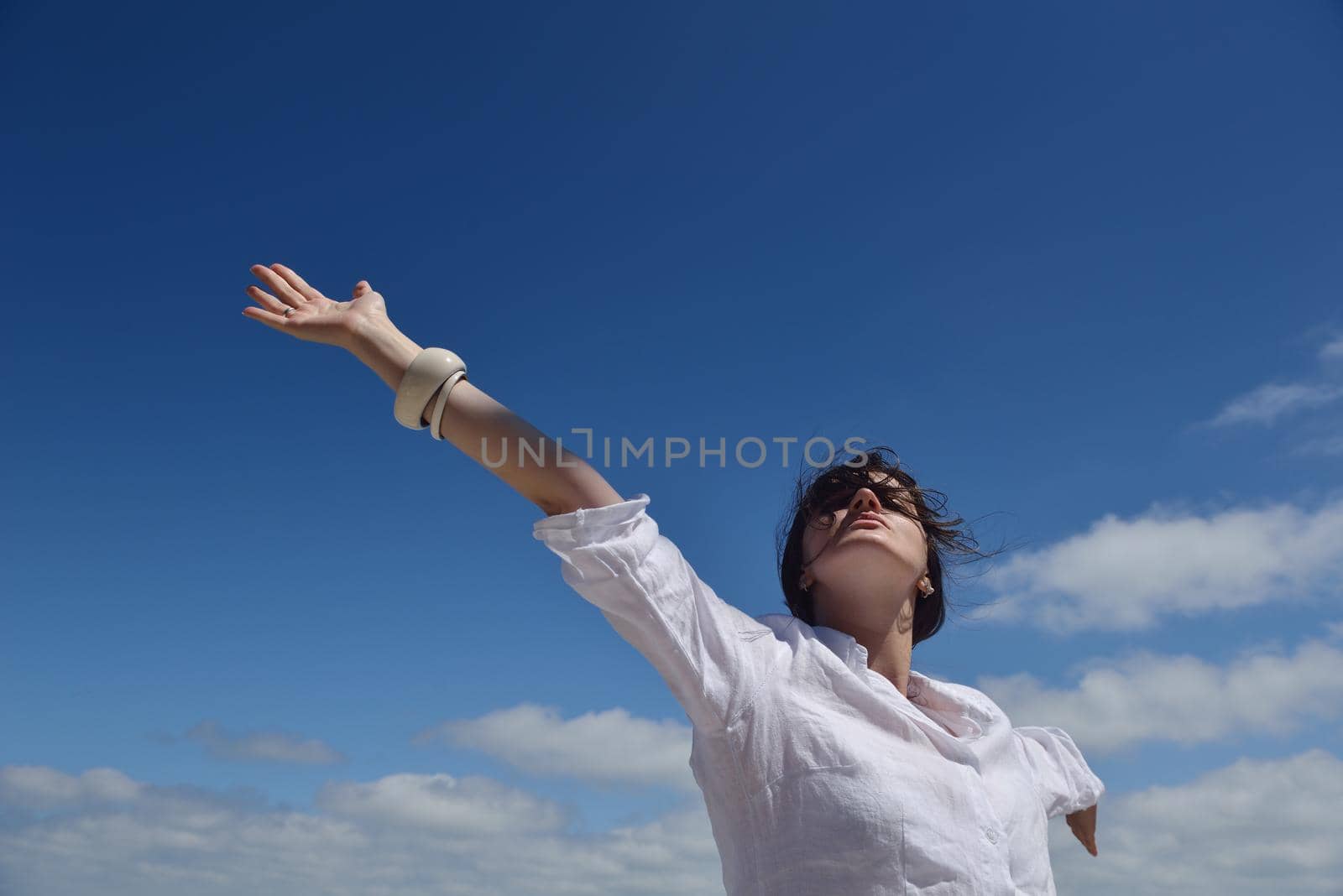 Happy  young woman with spreading arms, blue sky with clouds in background  - copyspace