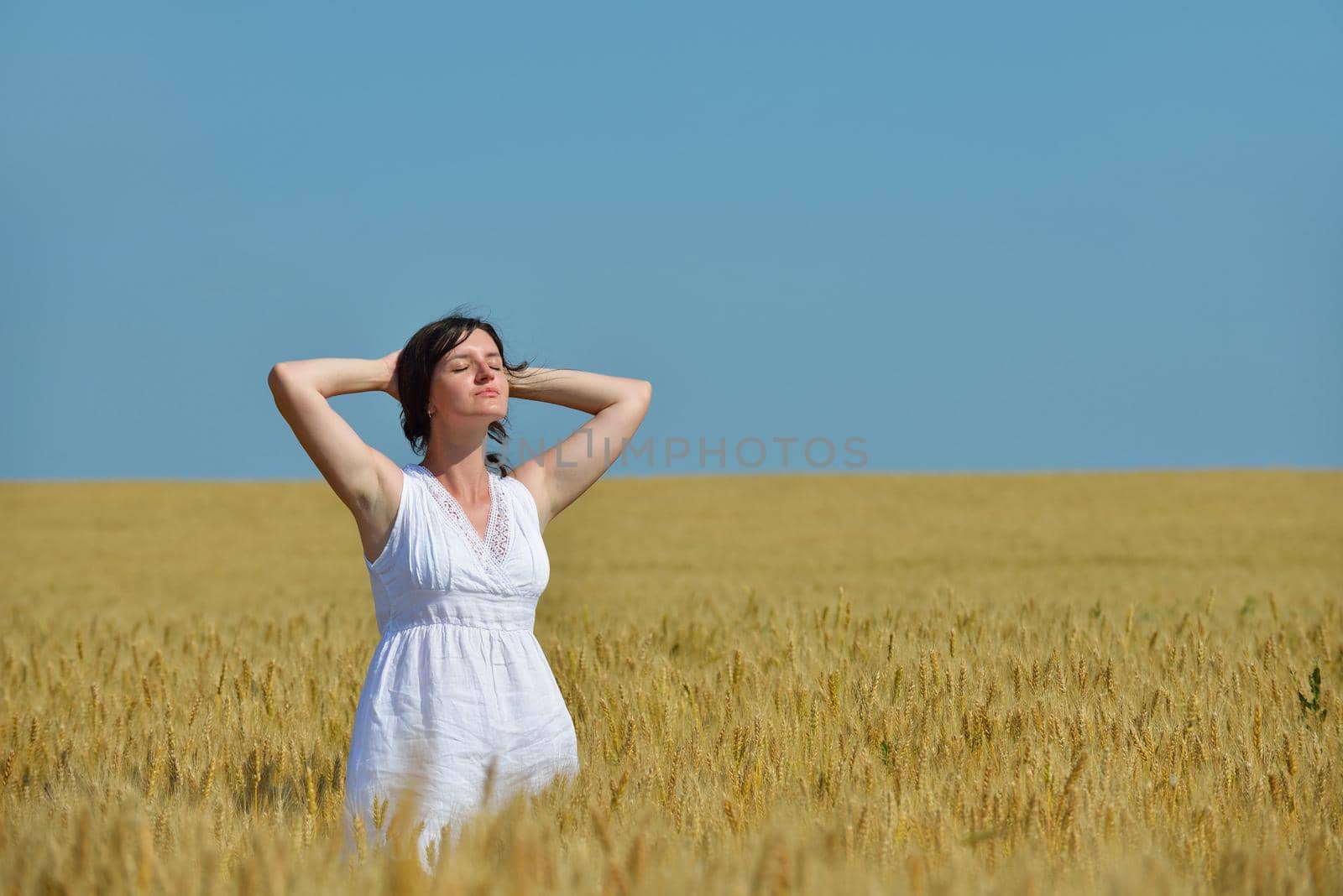 Young woman standing jumping and running  on a wheat field with blue sky in  background at summer day representing healthy life and agriculture concept