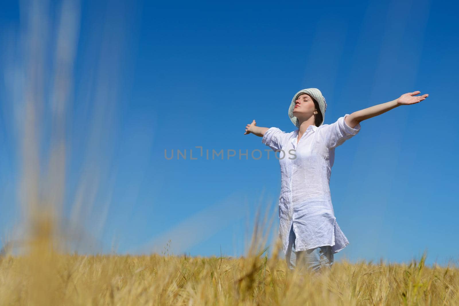 Young woman standing jumping and running  on a wheat field with blue sky in  background at summer day representing healthy life and agriculture concept