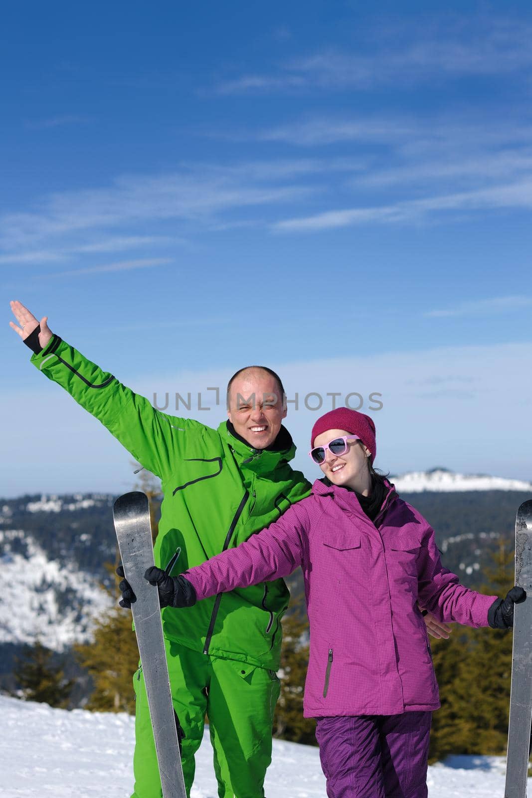 Portrait of happy couple at beautiful mountain on winter sunny day with blue sky and snow in background