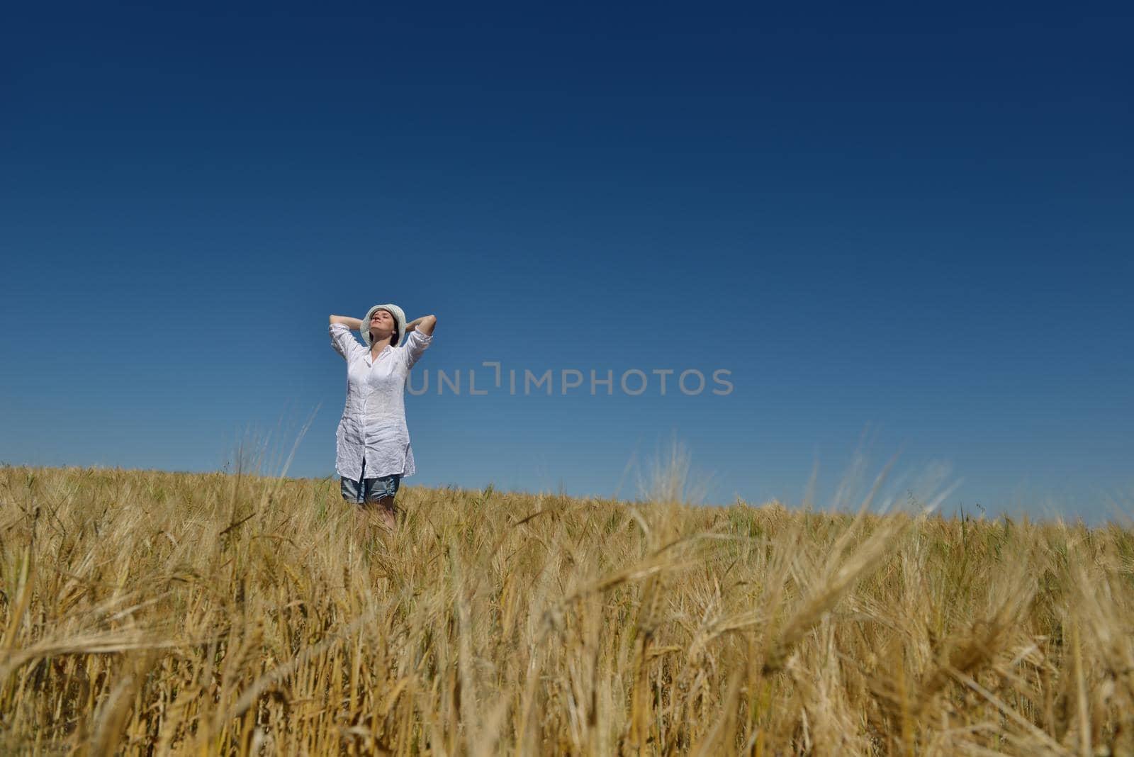 Young woman standing jumping and running  on a wheat field with blue sky the background at summer day representing healthy life and agriculture concept