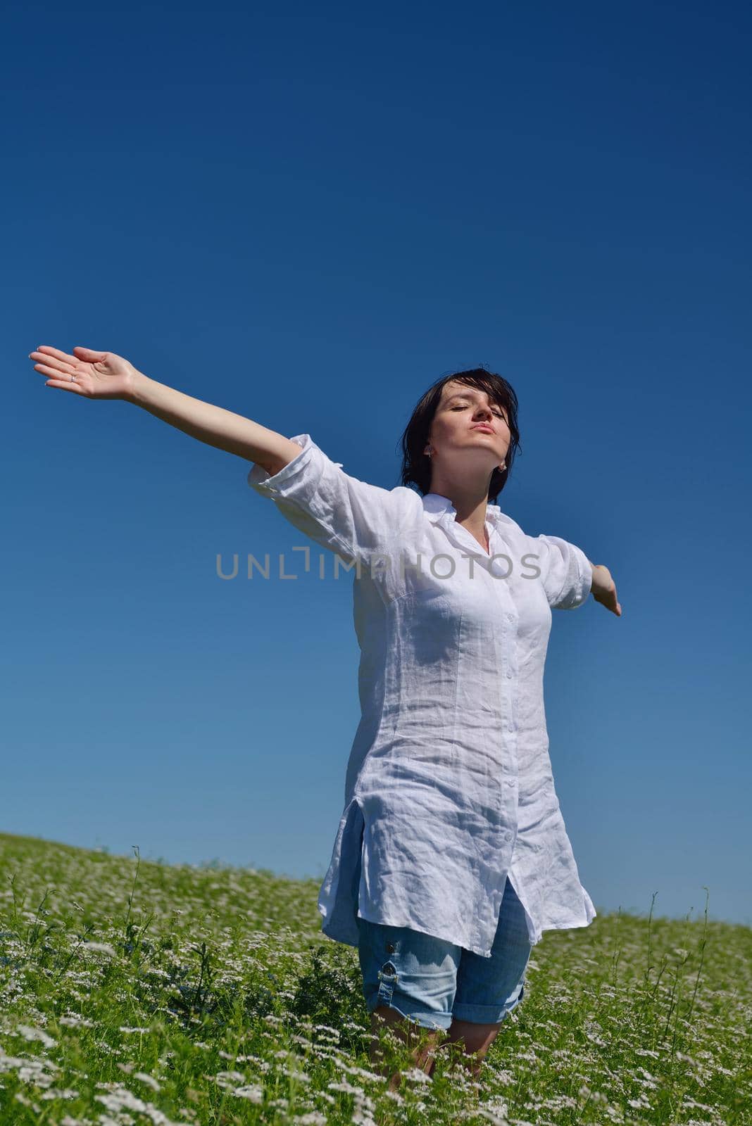 Young happy woman in green field with blue sky in background