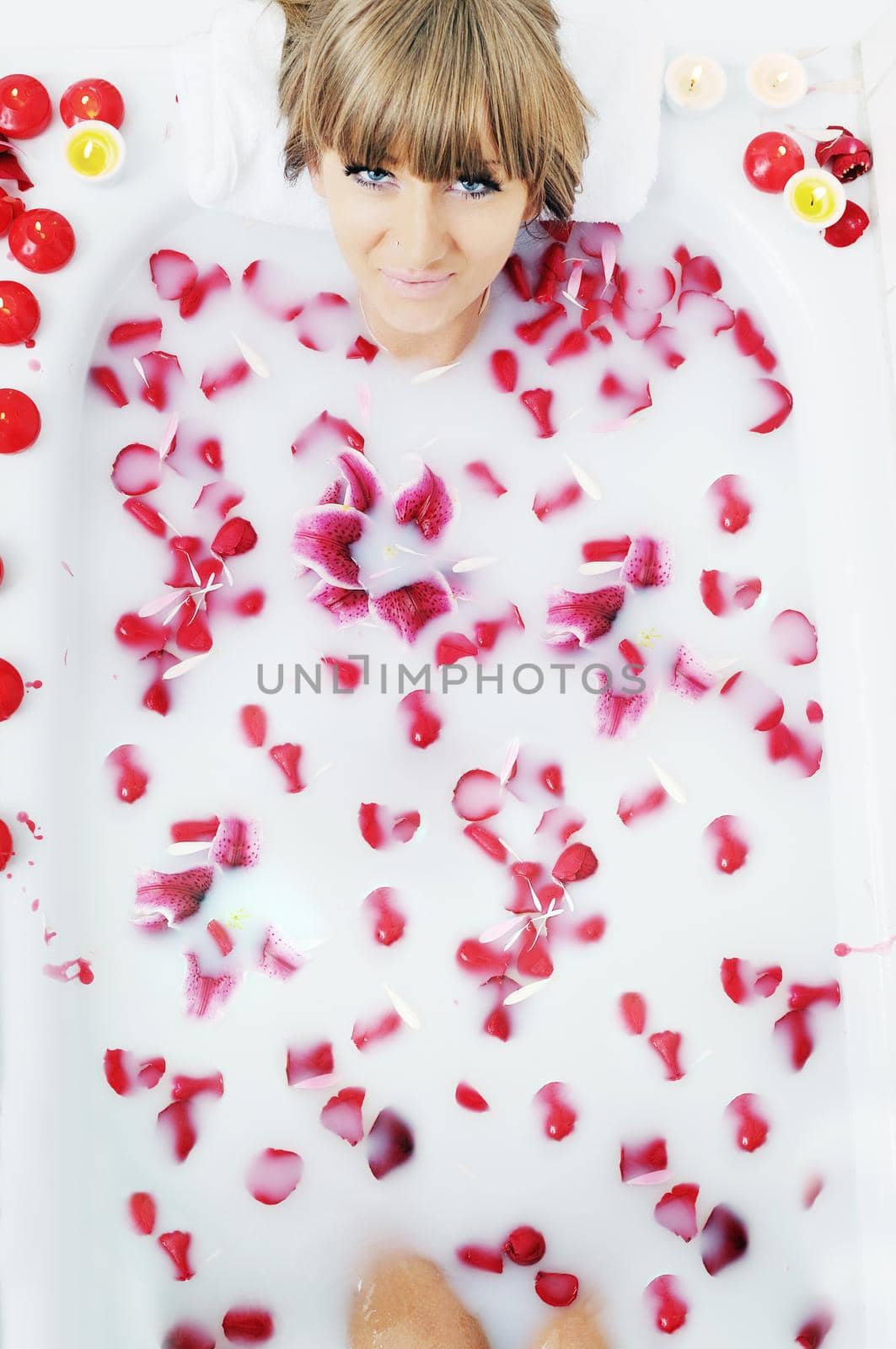 woman beauty spa and wellness treathment with red flower petals in bath with milk 