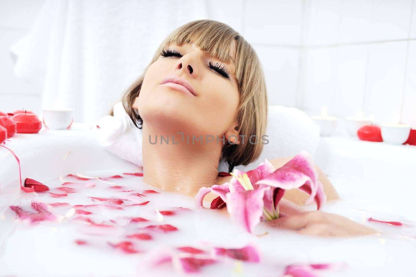 woman beauty spa and wellness treathment with red flower petals in bath with milk 