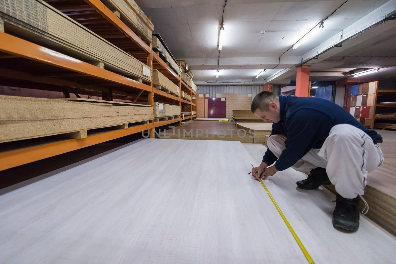 young man carpenter measuring wooden board for cutting while working in big modern carpentry High quality wood concept