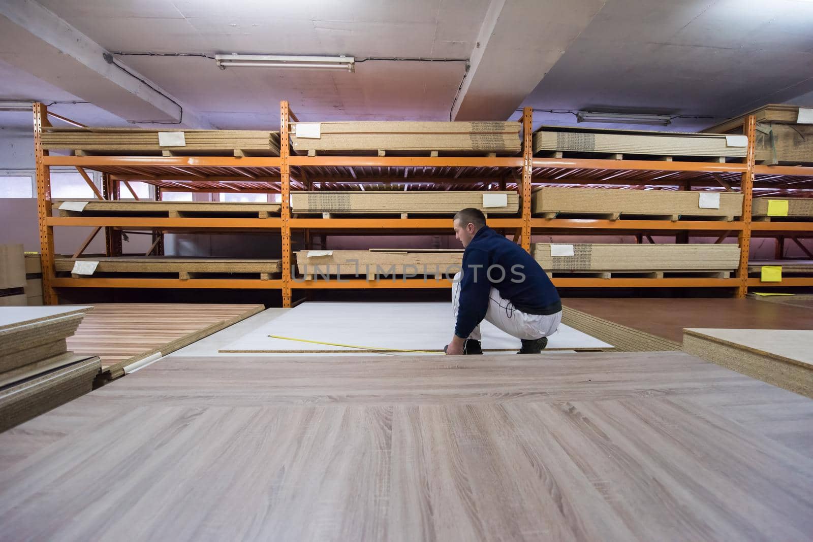 young man carpenter measuring wooden board for cutting while working in big modern carpentry High quality wood concept