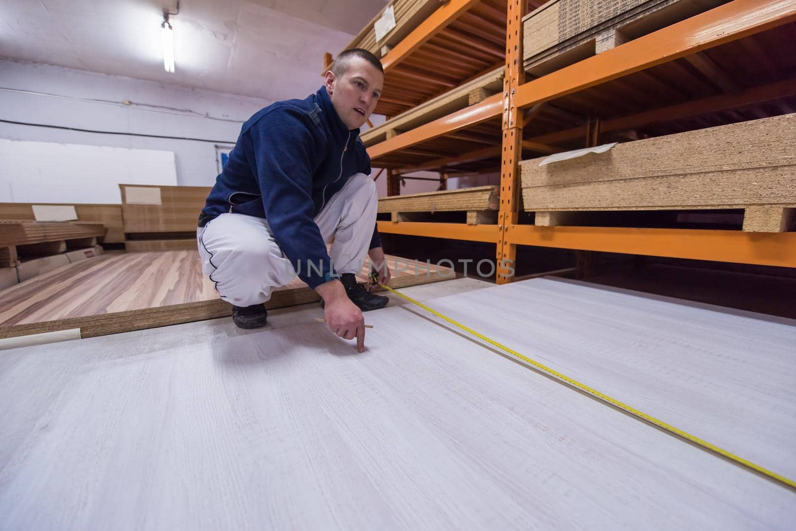 young man carpenter measuring wooden board for cutting while working in big modern carpentry High quality wood concept