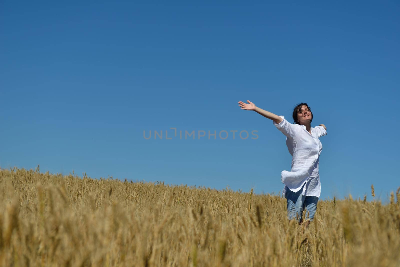 Young woman standing jumping and running  on a wheat field with blue sky the background at summer day representing healthy life and agriculture concept