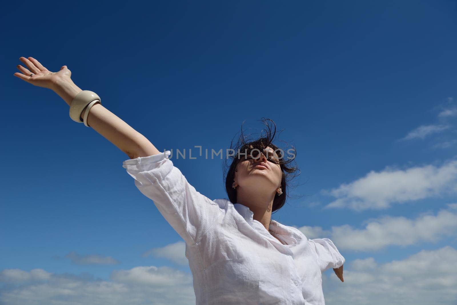 Happy  young woman with spreading arms, blue sky with clouds in background  - copyspace