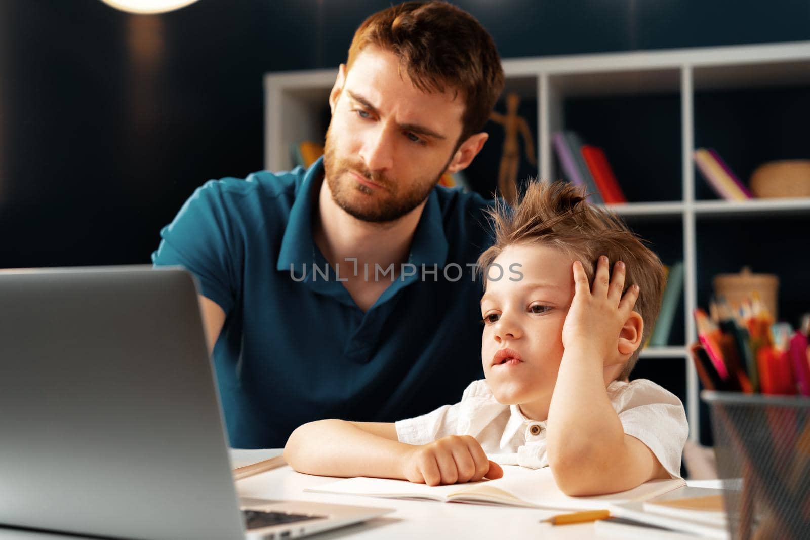 Young boy sitting with his father at the table and using laptop for study