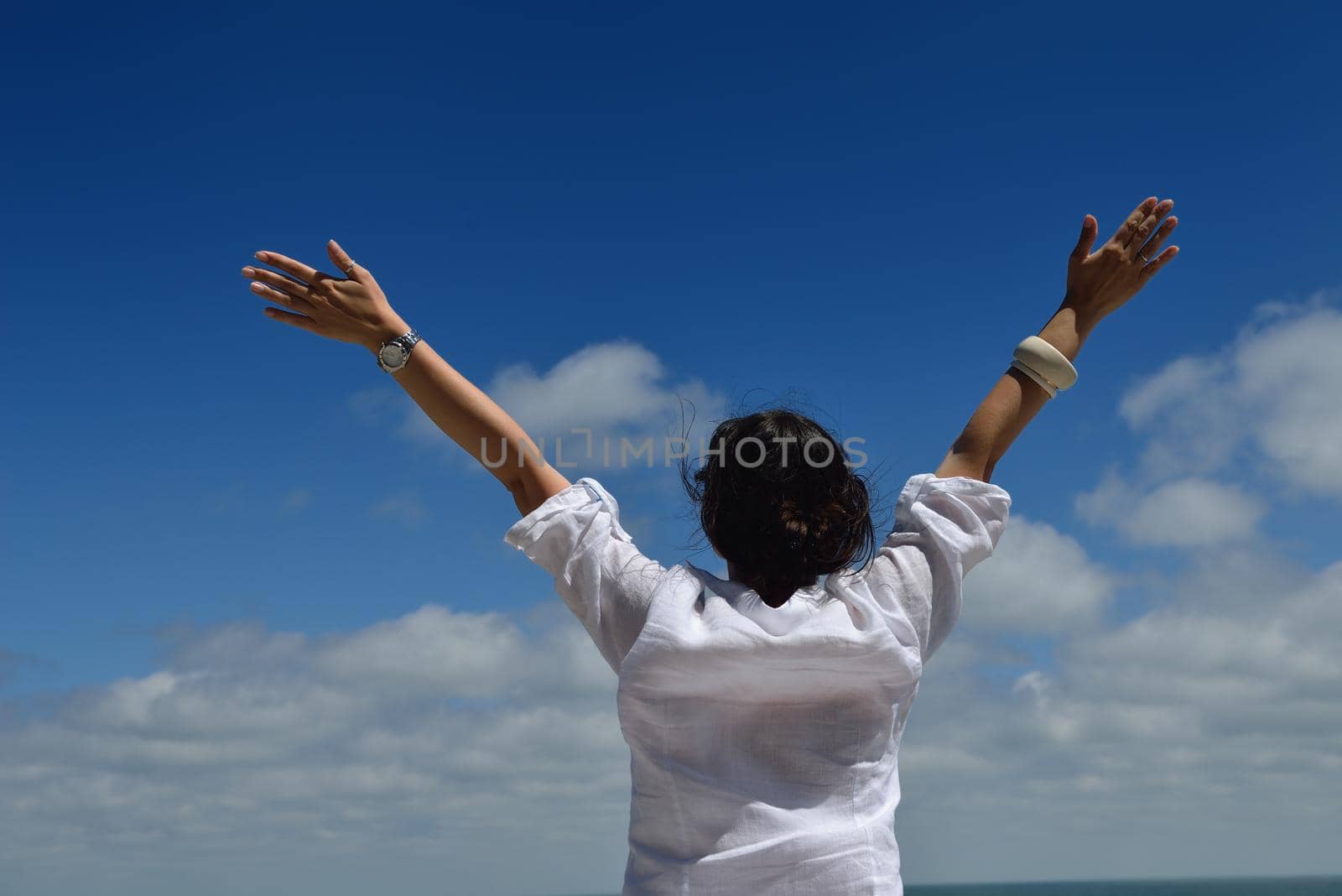 Happy  young woman with spreading arms, blue sky with clouds in background  - copyspace