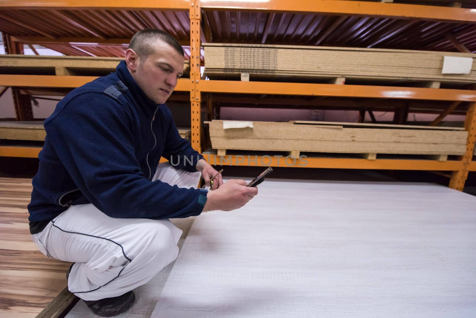 young man carpenter using a mobile phone to calculate measures for wooden board while working in big modern carpentry High quality wood concept