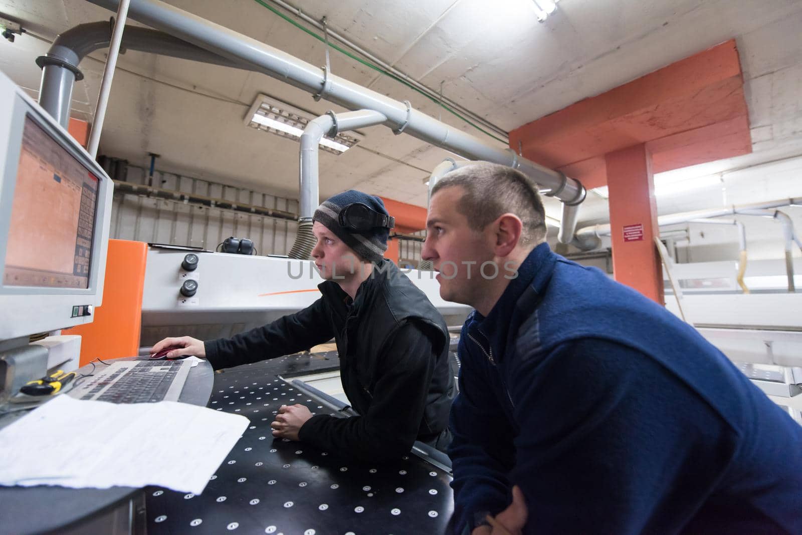 two young carpenters calculating and programming a cnc wood working machine in workshop. wood workers preparing a computer program for CNC machine at big modern carpentry