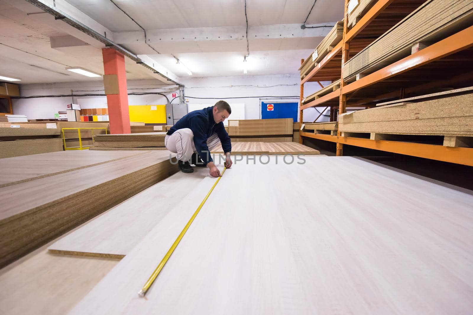 young man carpenter measuring wooden board for cutting while working in big modern carpentry High quality wood concept