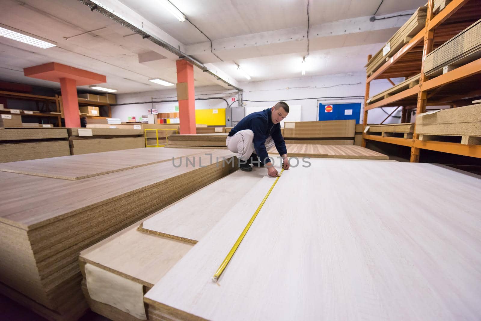 young man carpenter measuring wooden board for cutting while working in big modern carpentry High quality wood concept