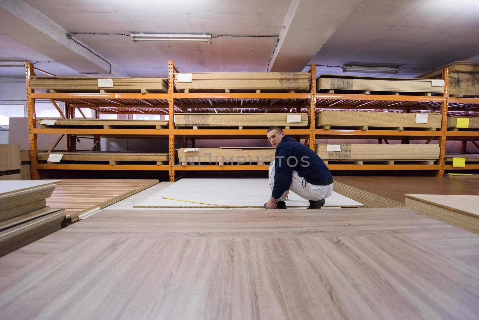 young man carpenter measuring wooden board for cutting while working in big modern carpentry High quality wood concept