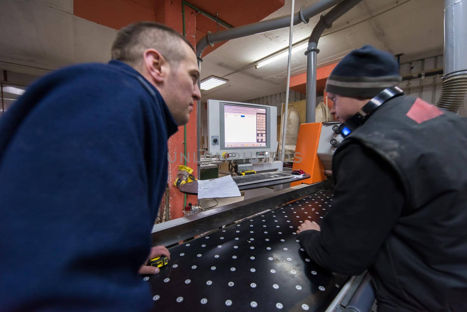 two young carpenters calculating and programming a cnc wood working machine in workshop. wood workers preparing a computer program for CNC machine at big modern carpentry