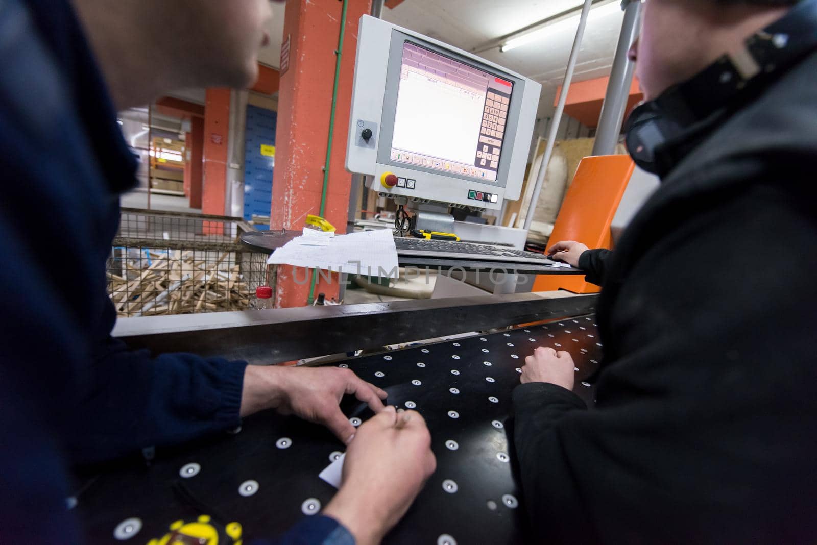 two young carpenters calculating and programming a cnc wood working machine in workshop. wood workers preparing a computer program for CNC machine at big modern carpentry