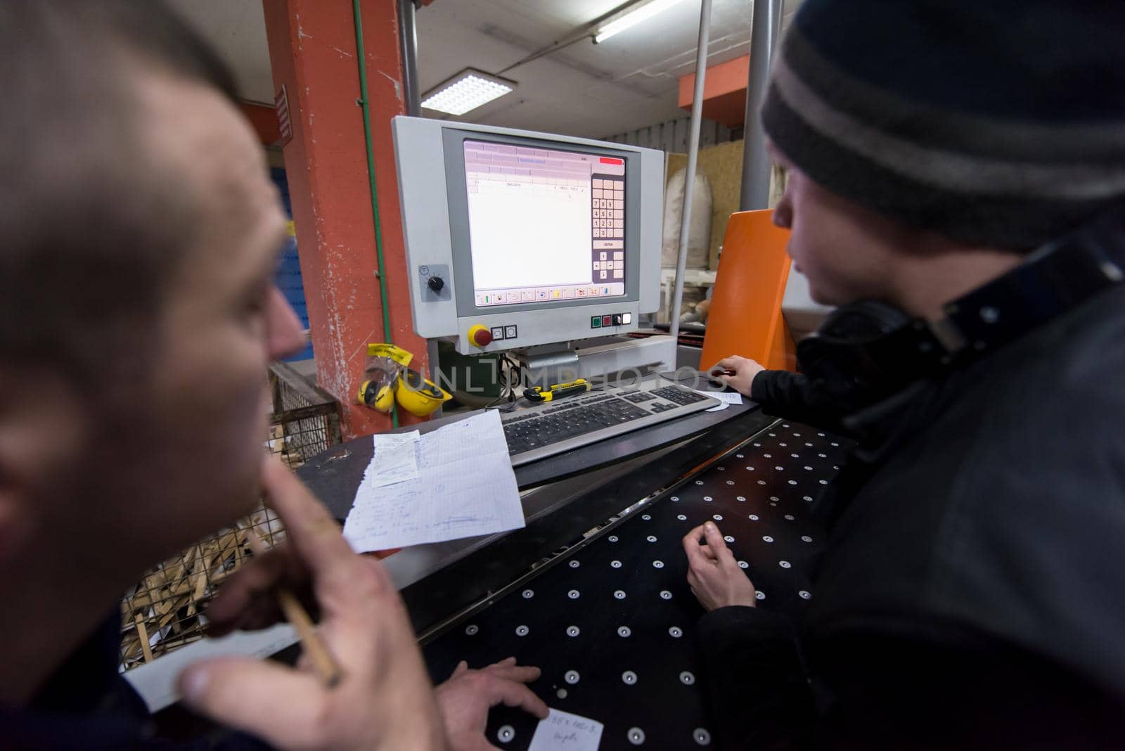 two young carpenters calculating and programming a cnc wood working machine in workshop. wood workers preparing a computer program for CNC machine at big modern carpentry