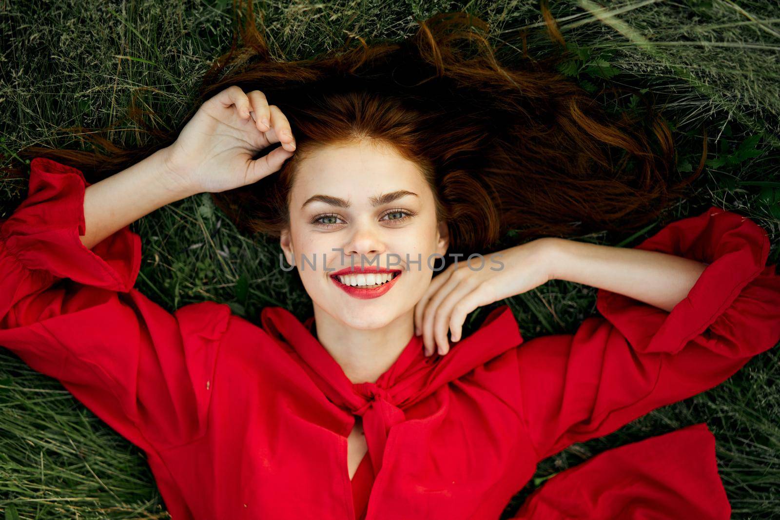 cheerful woman in a red dress lies on the grass top view. High quality photo