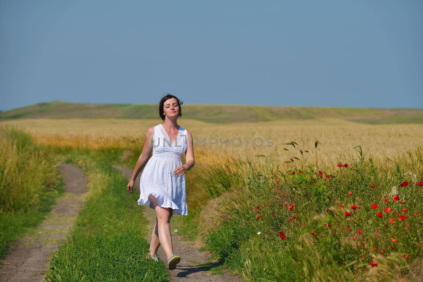 Young woman standing jumping and running  on a wheat field with blue sky in  background at summer day representing healthy life and agriculture concept